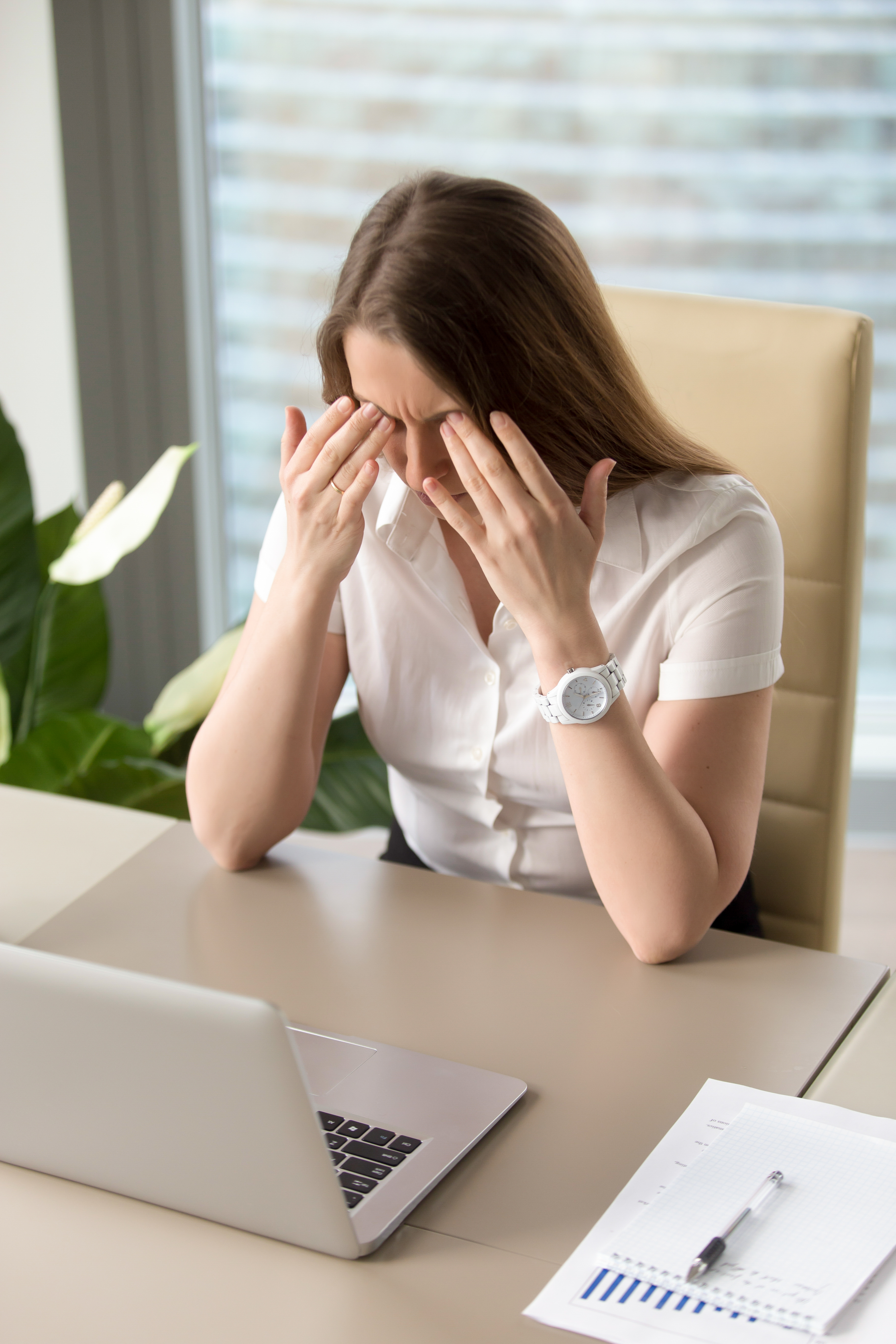 Stressed office worker holding her head in frustration at her desk.